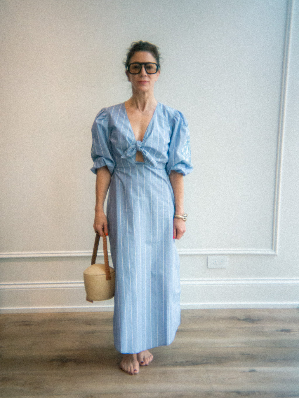 Woman wearing a light blue striped dress holding a beige canvas statement bag indoors.