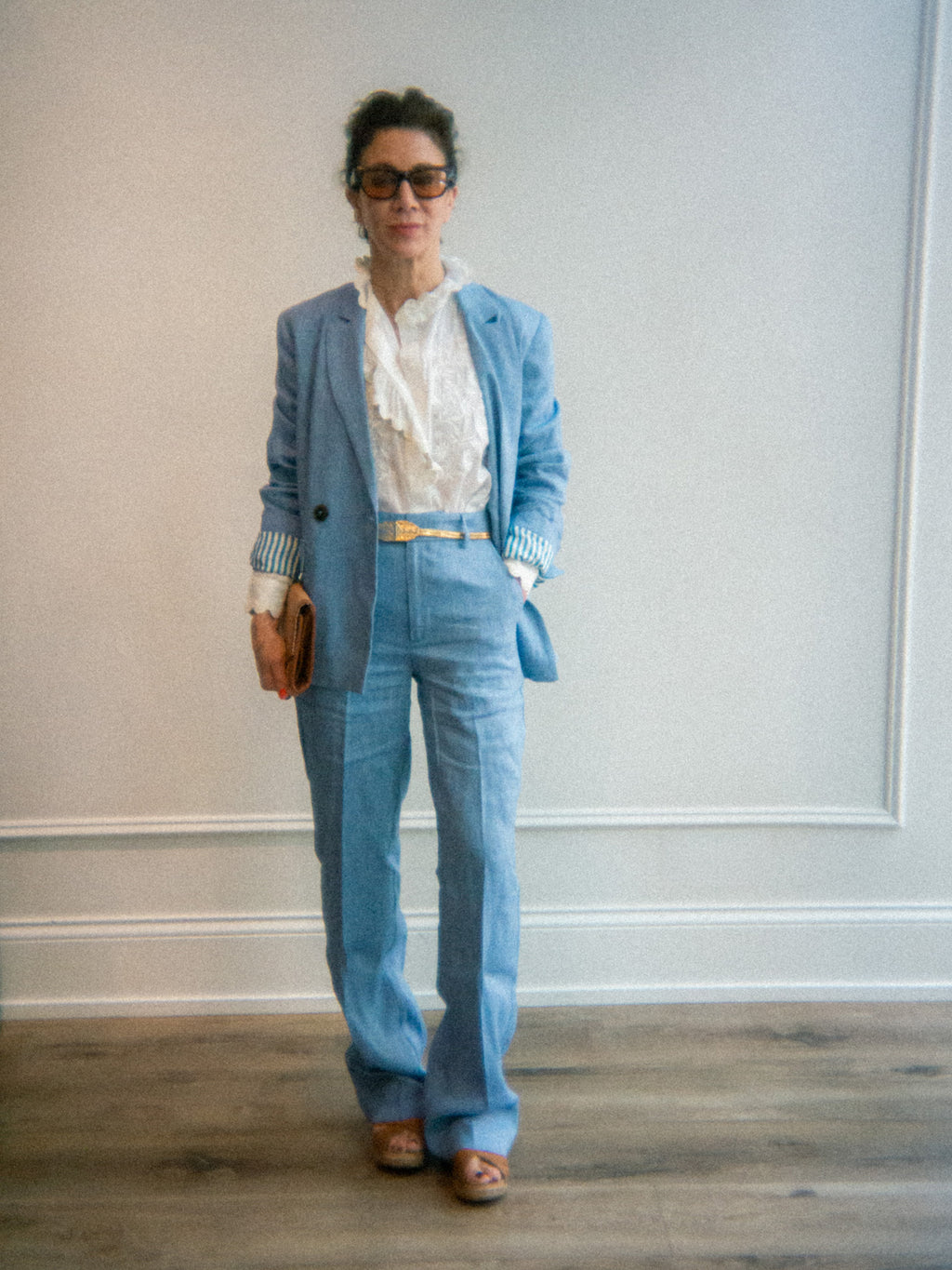 Person wearing a light blue summer suit set with a white button up shirt and sunglasses indoors.