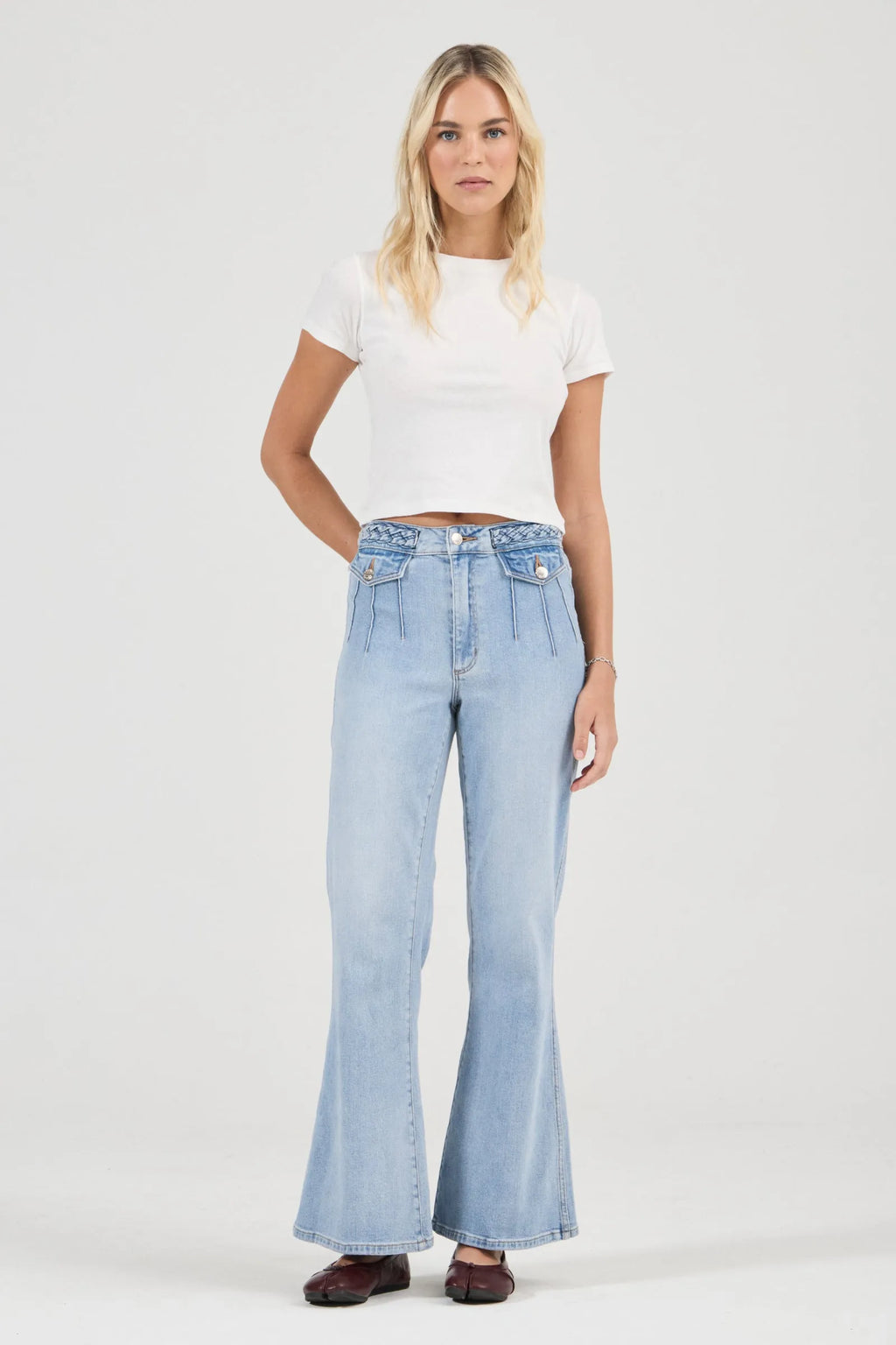 Woman wearing light blue flared jeans and a white top on a white background