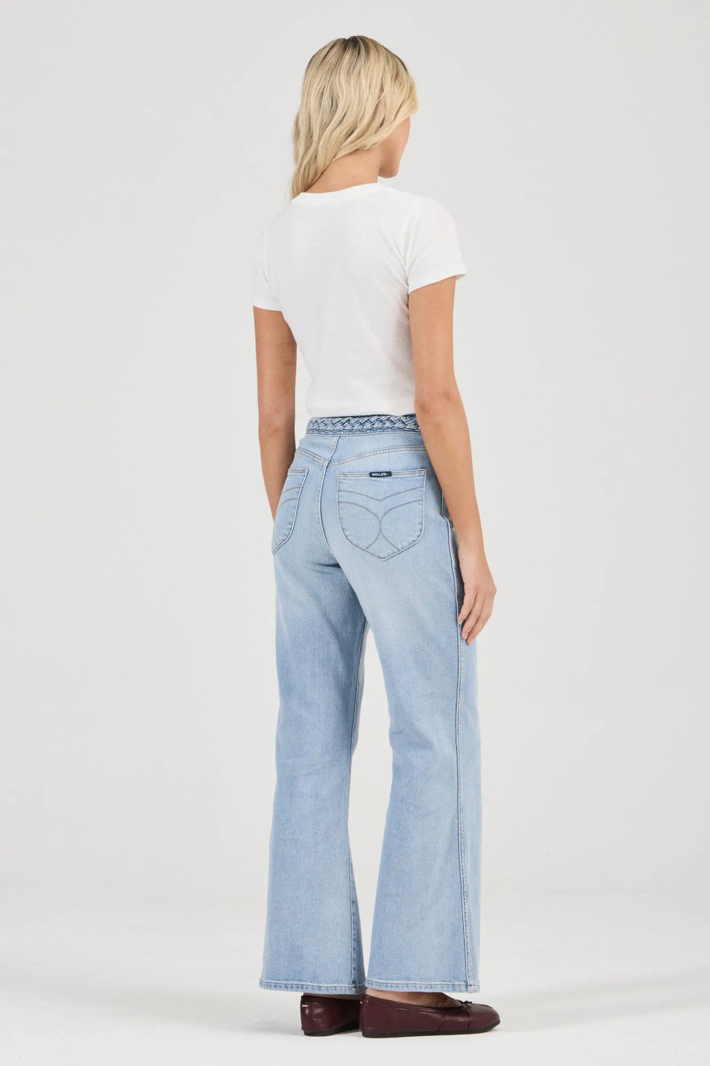 Woman wearing light blue flared jeans and a white top on a white background