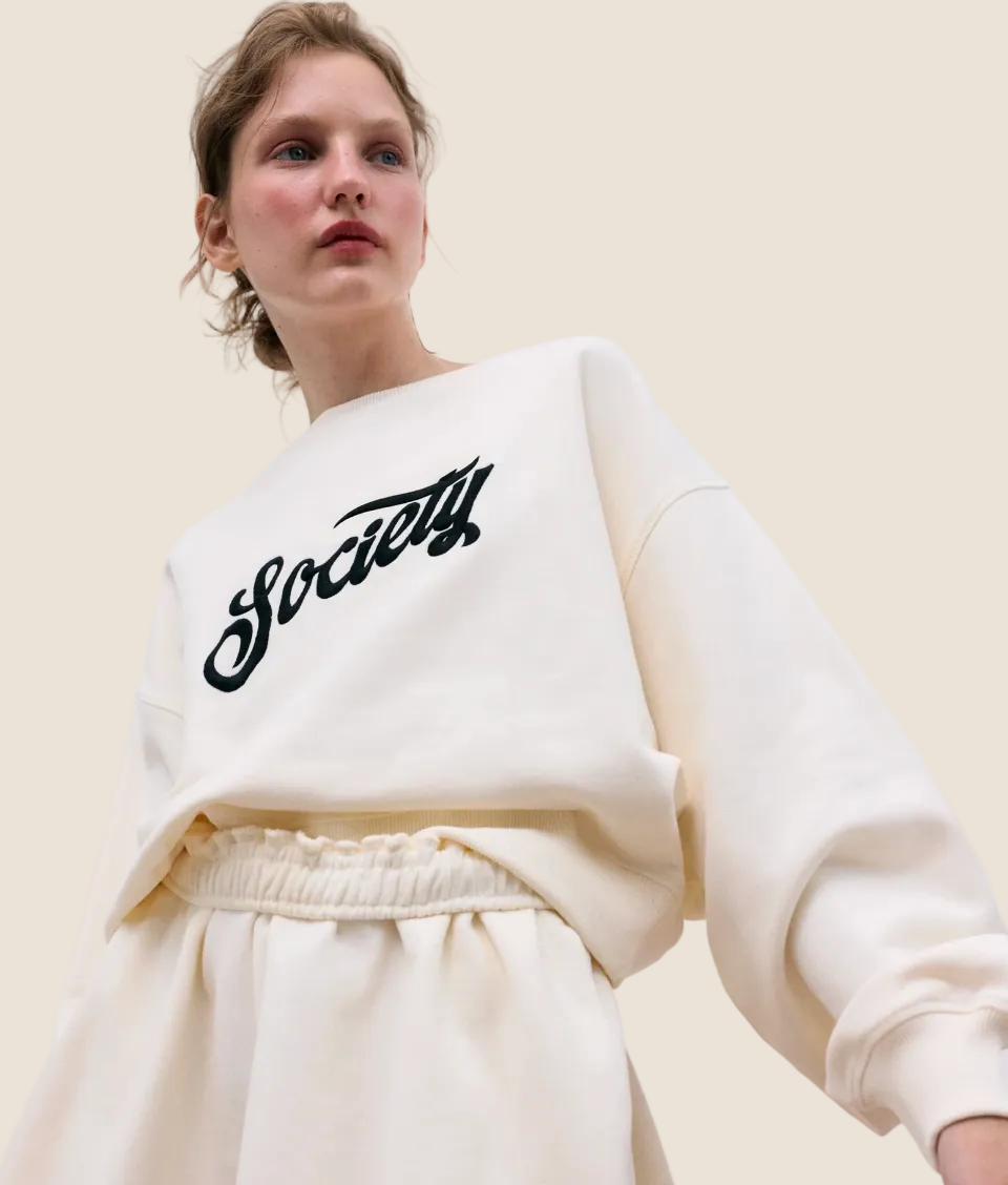 Person wearing a white sweatshirt with 'Society' text on a plain background