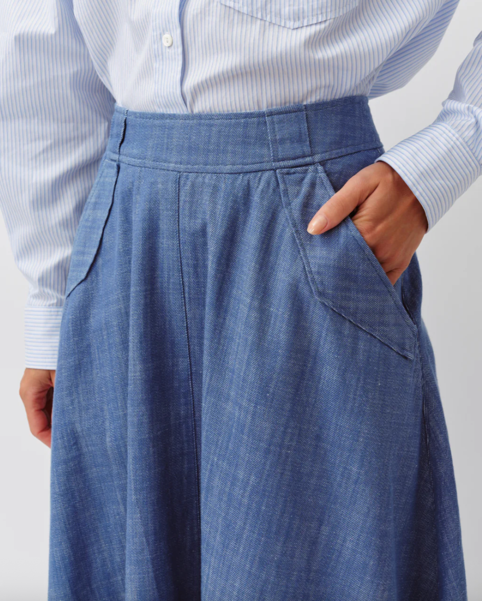 Person wearing a light blue striped shirt and blue pleated pants against a white background