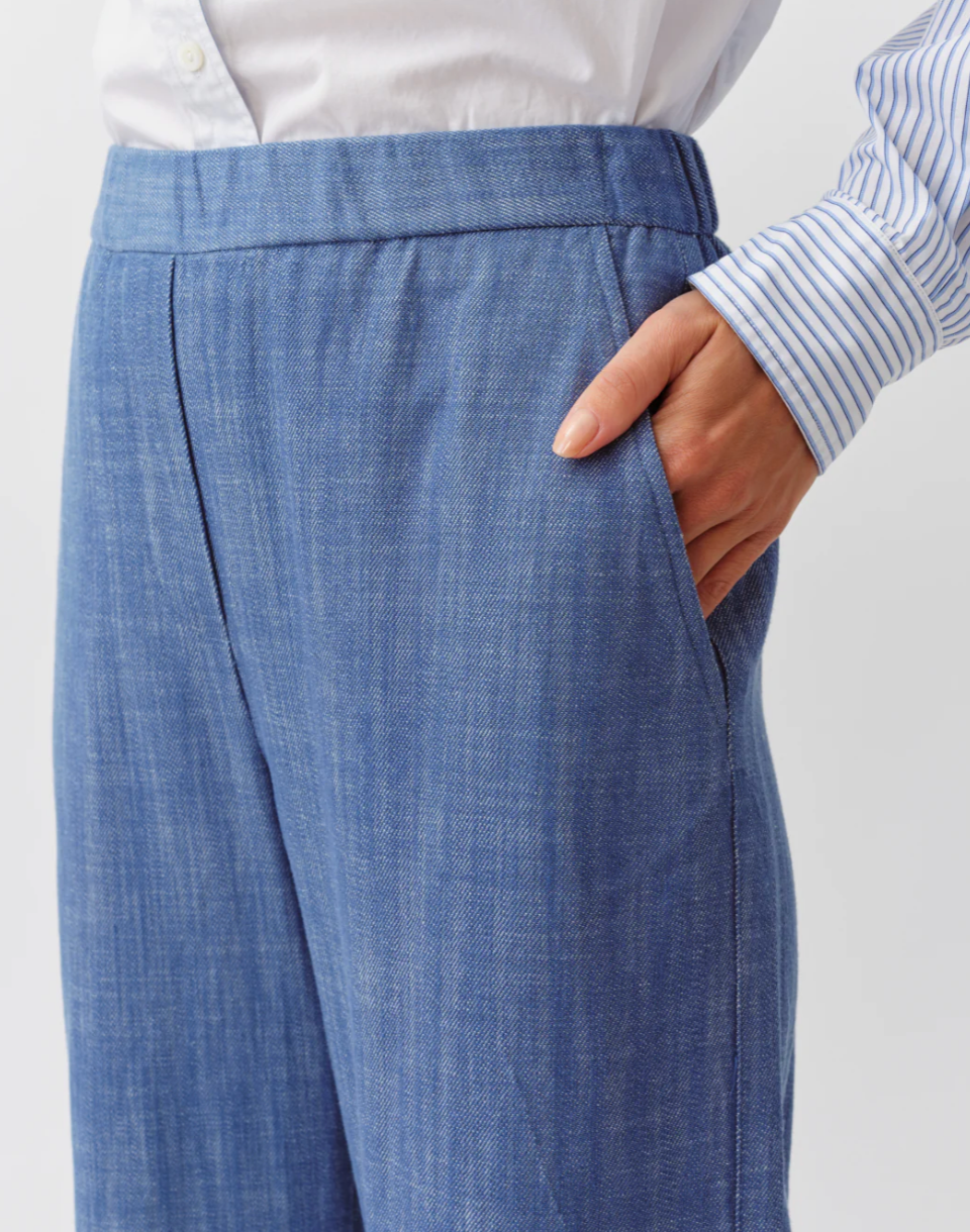 Blue pleated pants worn by a person on a white background