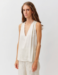 Woman wearing a white sleeveless top with a plain background