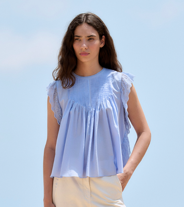 Woman wearing a light blue blouse with ruffled sleeves against a clear blue sky.