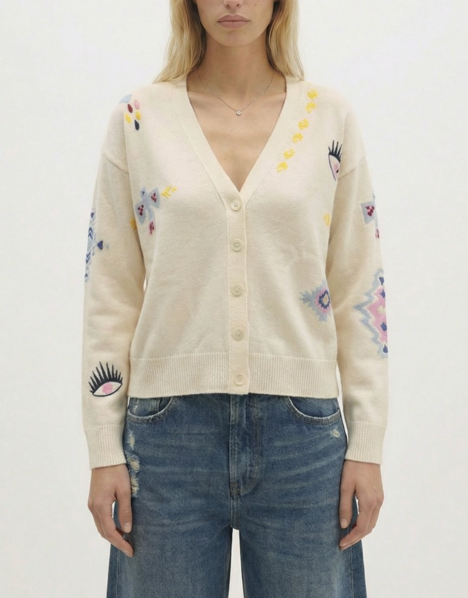 Person wearing a cream cardigan with floral and eyelash designs on a white background