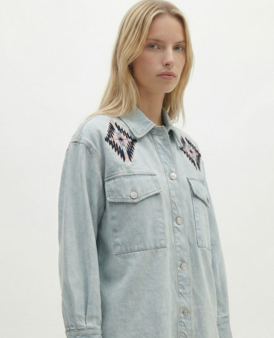 Woman wearing a light blue denim jacket with embroidered designs on a white background
