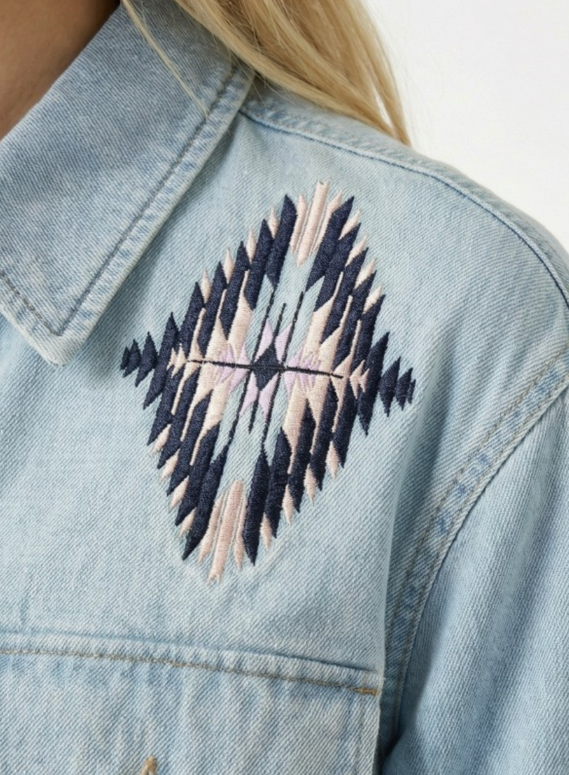 Light blue denim jacket with a geometric embroidered design on the chest.