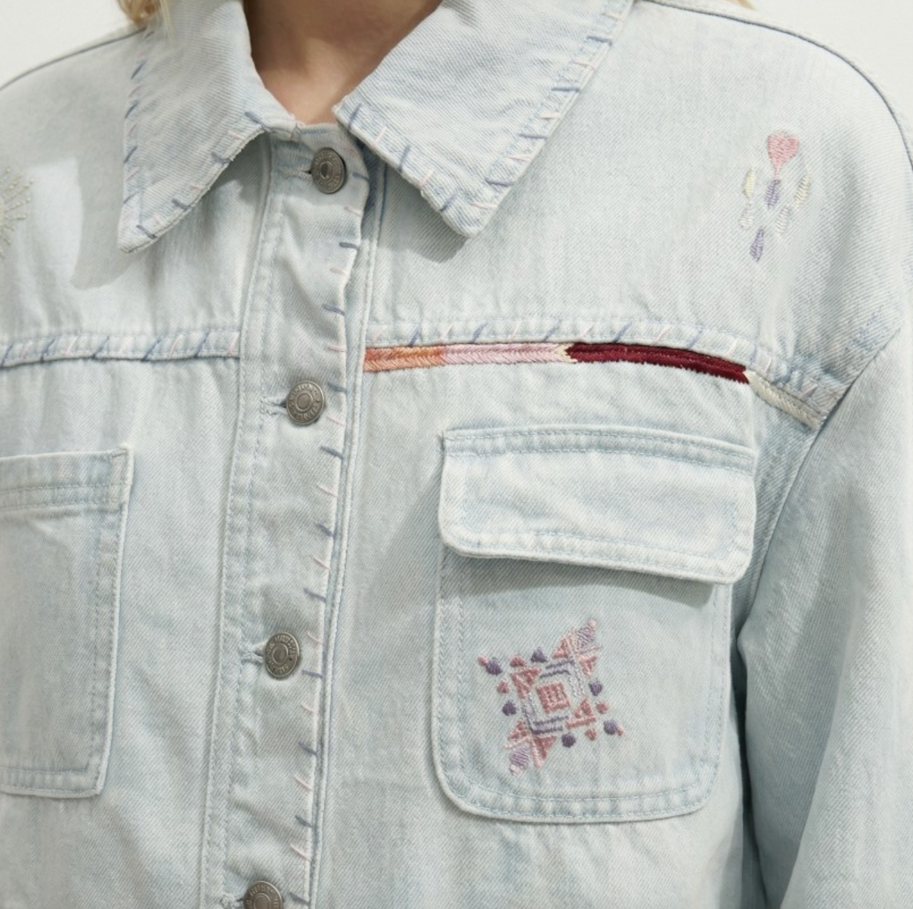 Light blue denim jacket with embroidered designs on a plain background