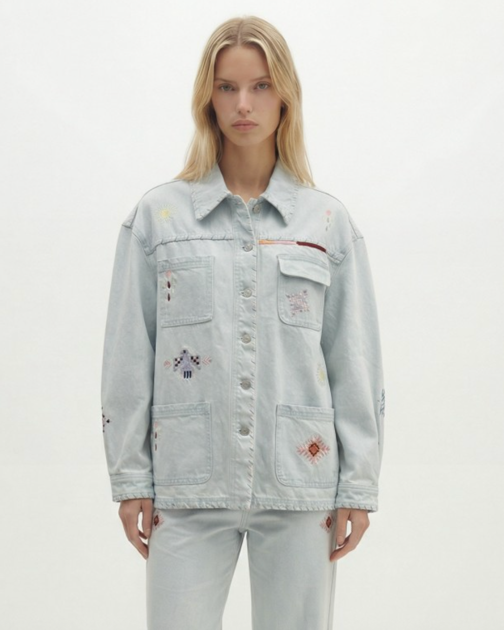 Person wearing a light blue denim jacket with floral embroidery on a white background