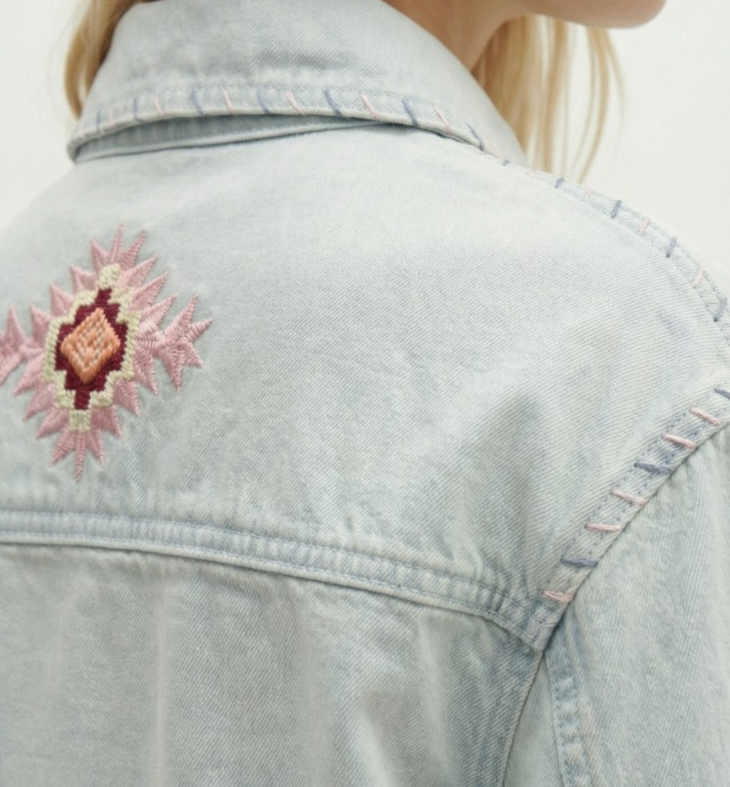 Light blue denim jacket with a pink floral embroidery on the shoulder.