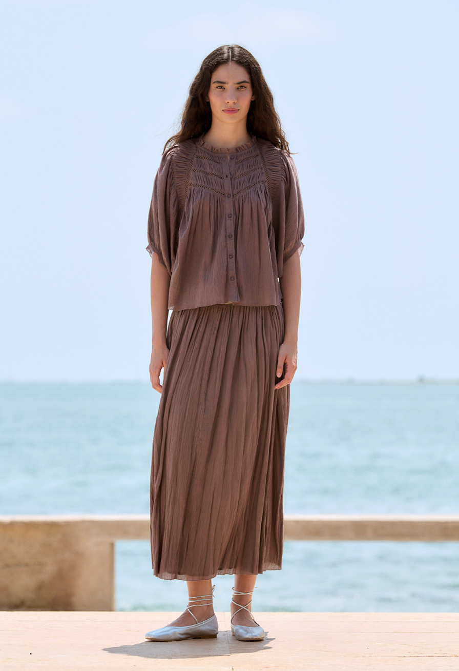 Woman wearing a brown outfit standing by a body of water. Mocha Skirt and Mocha shirt for spring, mocha chocolate color for spring 