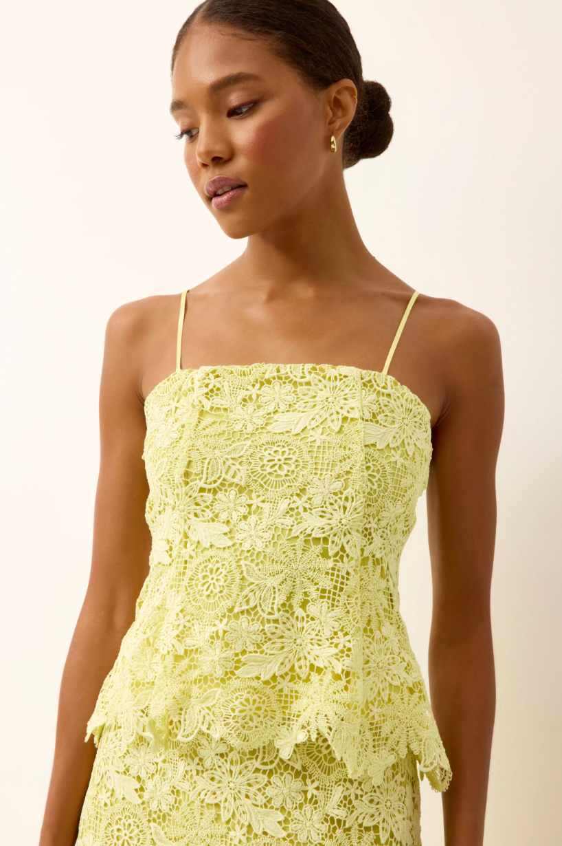Woman wearing a light yellow lace dress against a plain background