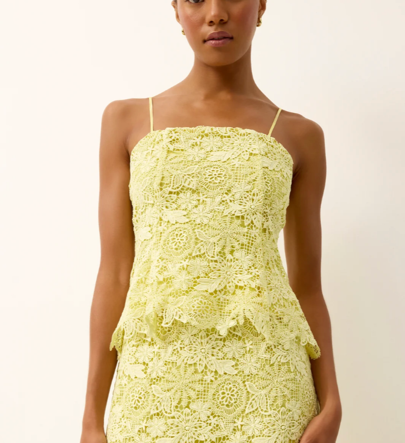 Woman wearing a light yellow lace dress against a plain background