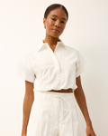 Woman wearing a white blouse and pants against a plain background