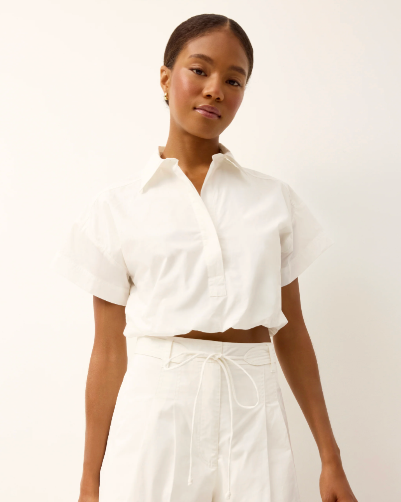 Woman wearing a white blouse and pants against a plain background