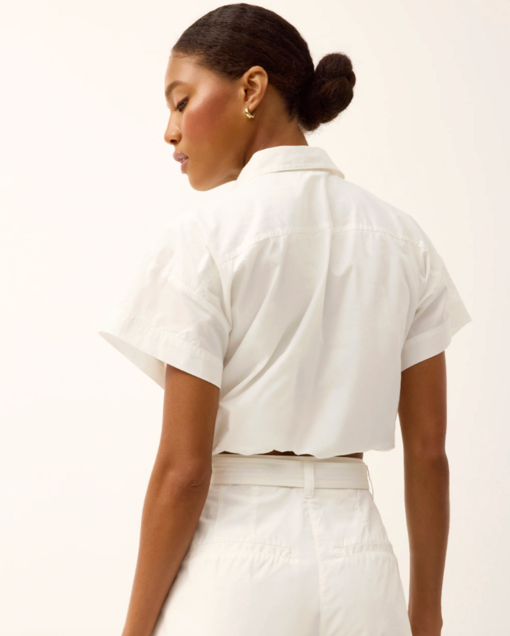 Woman wearing a white cropped shirt and pants against a plain background