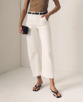 Person wearing white barrel pants and a brown top on a plain background