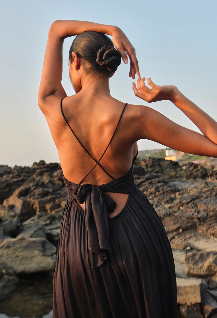 Woman in a dark dress standing on a rocky beach with a blurred background