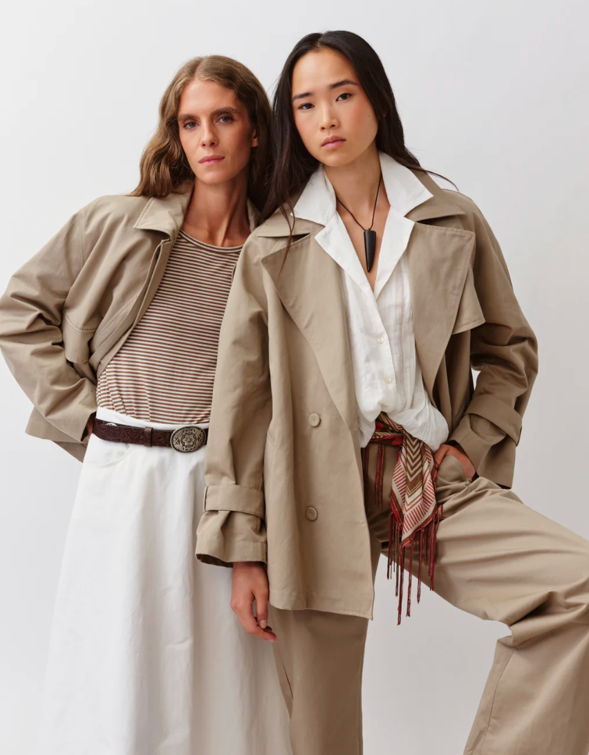 Two women wearing cropped beige trench coats against a white background
