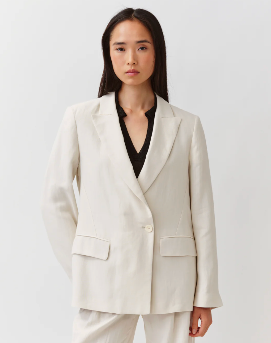 Woman wearing a light beige blazer over a black top on a white background