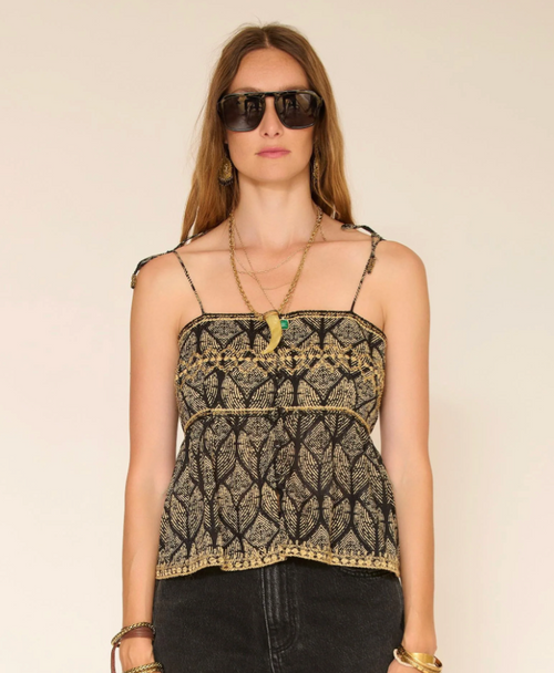 Woman wearing a black and gold patterned top with sunglasses on a beige background
