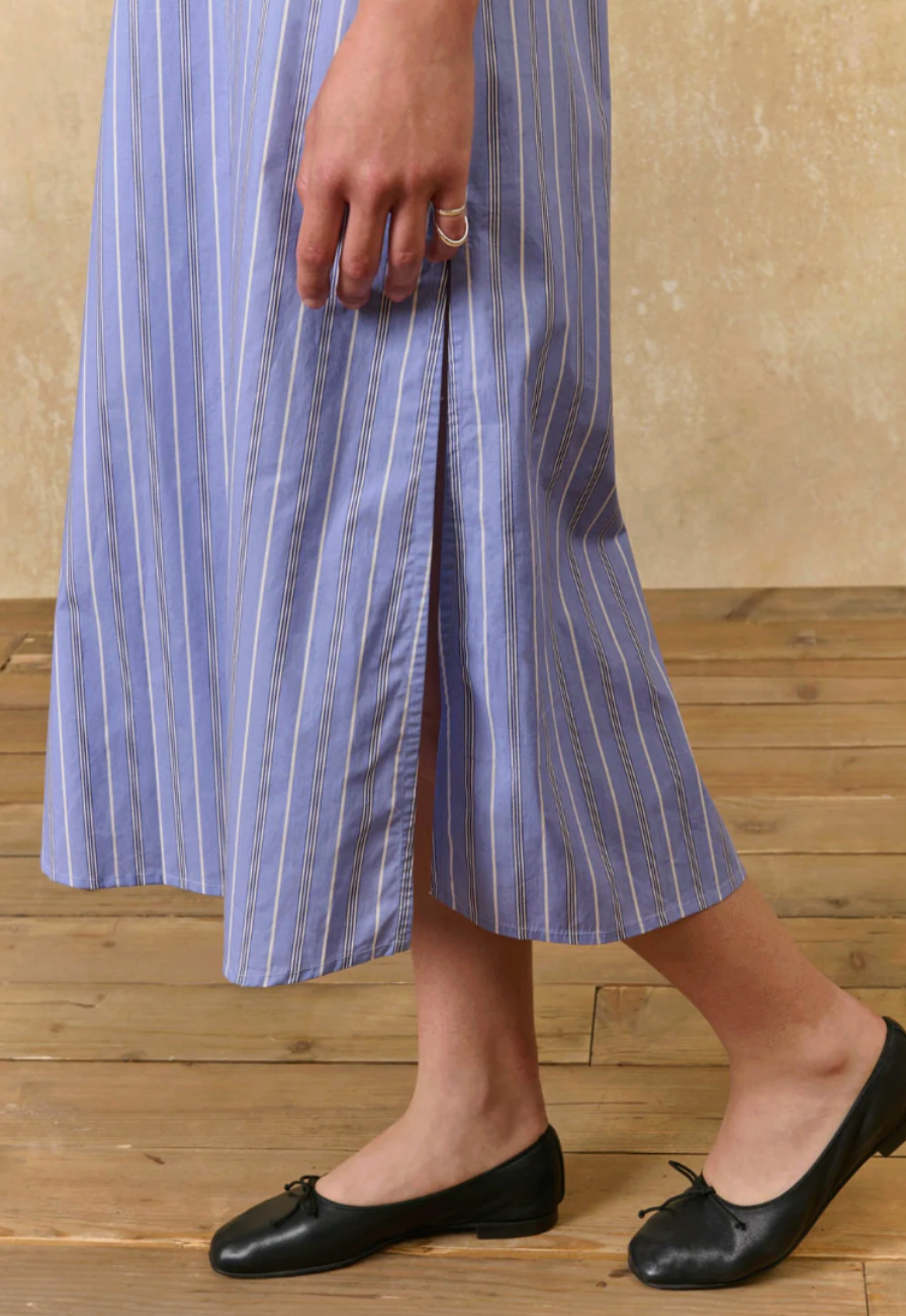Person wearing a blue and white striped dress with black flats on a wooden floor.