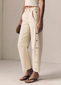Person wearing beige pants with button details on a plain background
