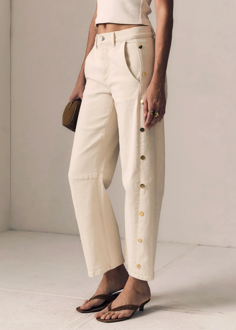 Person wearing beige pants with button details on a plain background