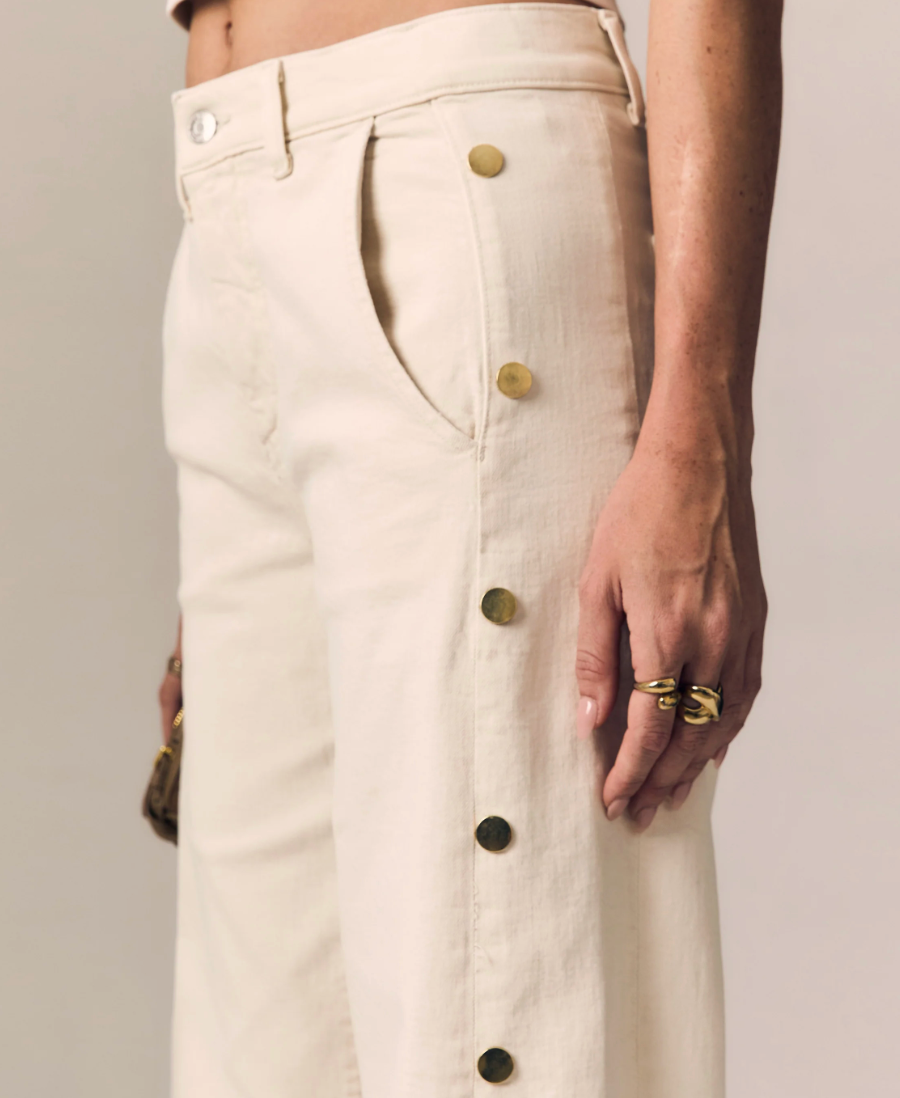 Beige pants with gold buttons worn by a person on a neutral background