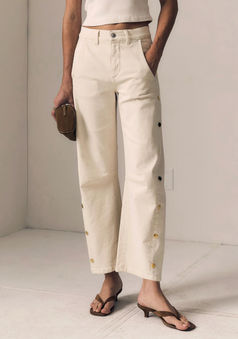 Person wearing beige pants with button details against a plain background