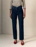 A model wearing dark blue straight-leg denim jeans, a black and white striped long-sleeve top, and red pointed-toe heels, standing against a plain off-white studio background.