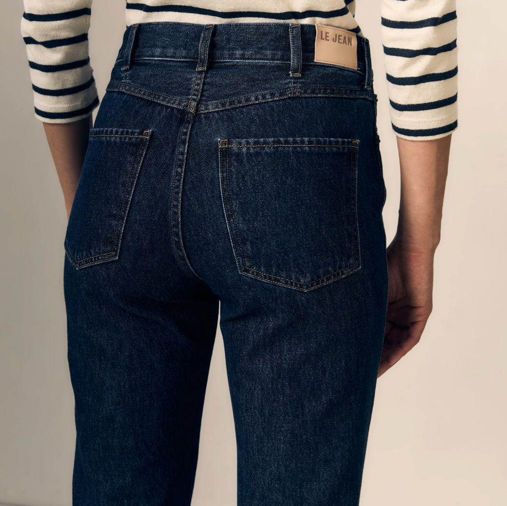 Rear view of a person wearing dark blue denim jeans with a striped long-sleeve shirt, showing the back pockets and waistband of the jeans.