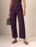 A model wearing a pair of dark purple cropped wide-leg pants, styled with a brown top, black flip-flops, and holding a brown woven handbag against a plain beige studio background.