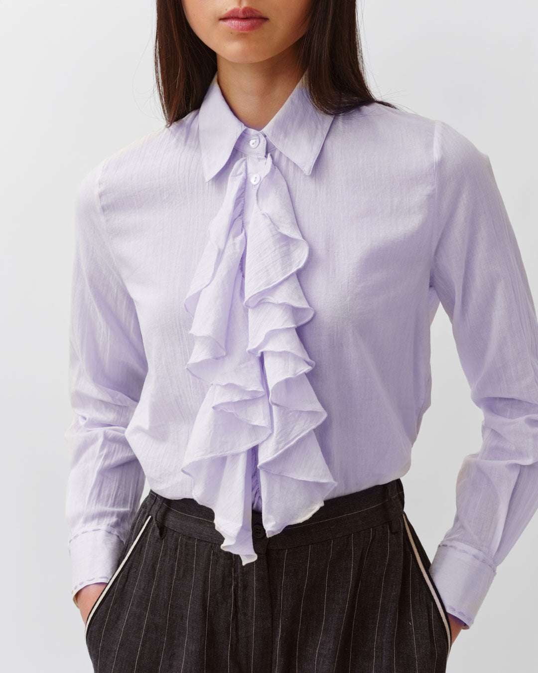 Light purple blouse with ruffled details worn by a person on a plain background