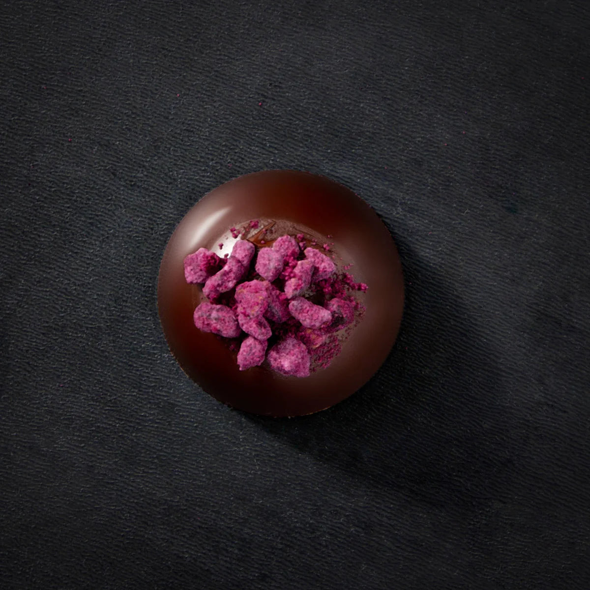 Chocolate truffle with pink toppings on a dark surface