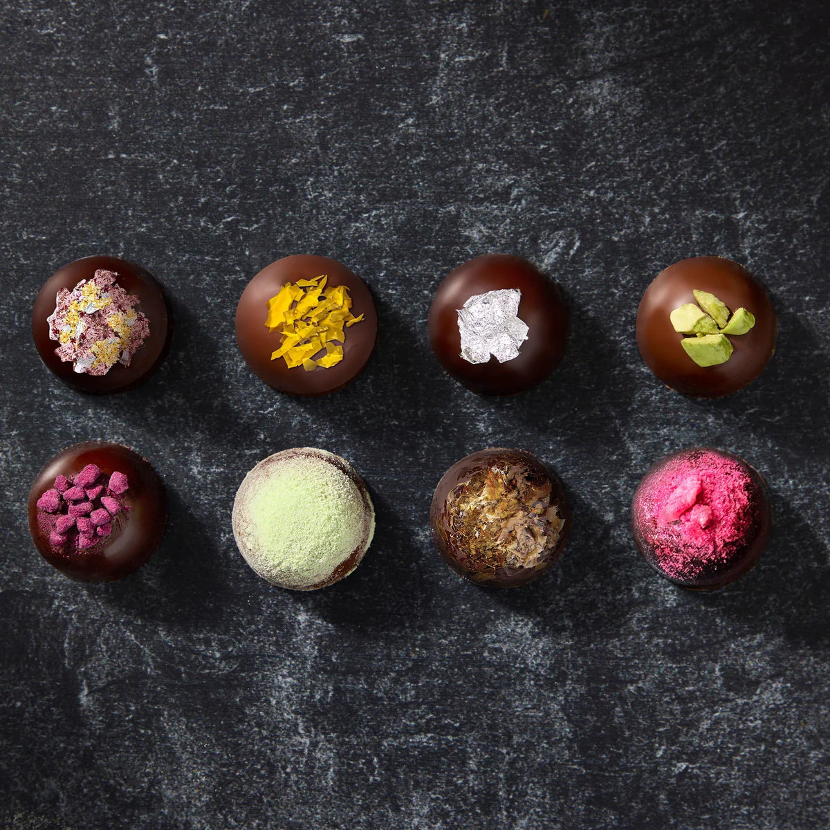 Assorted chocolate truffles with various toppings on a dark surface