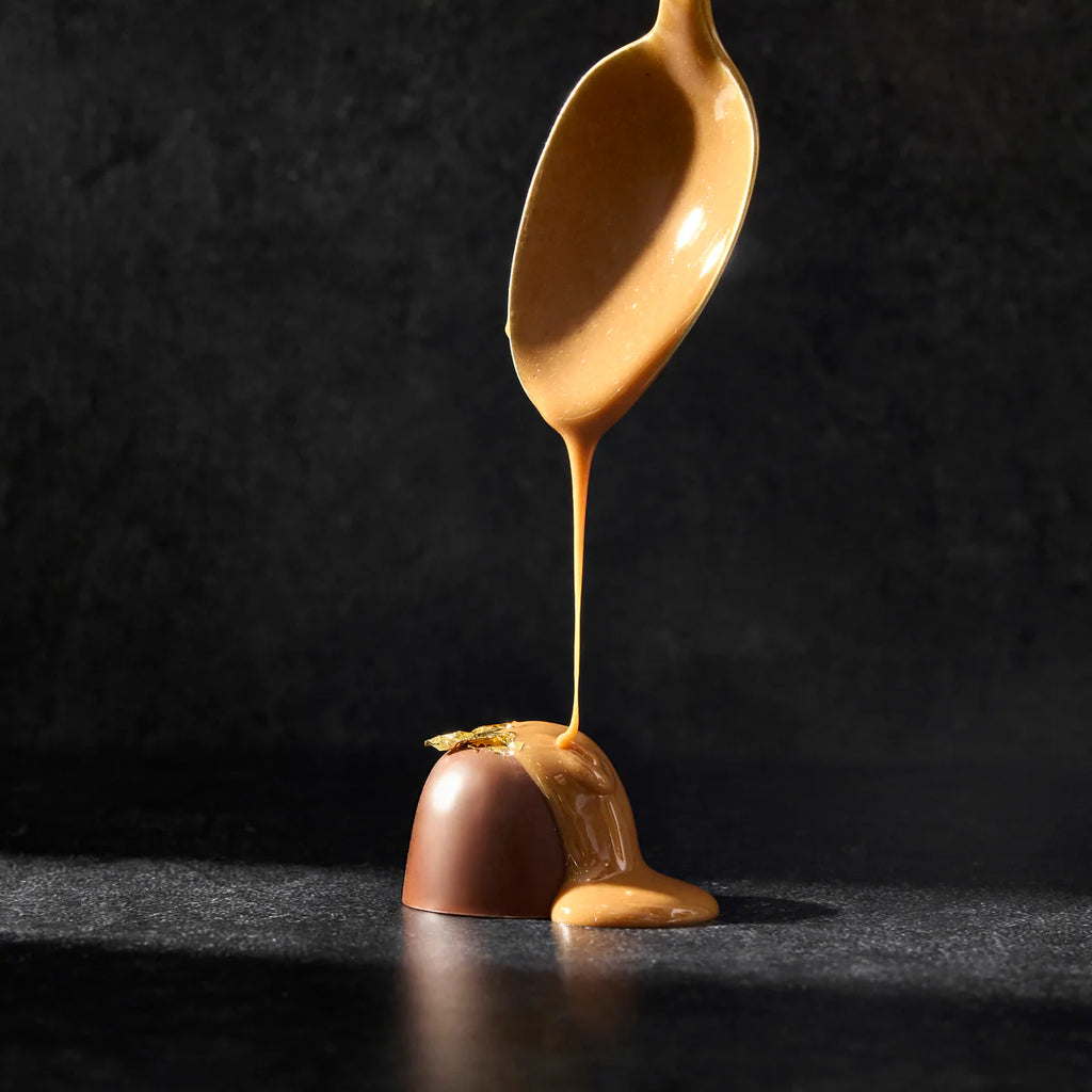Spoon drizzling caramel onto a chocolate truffle against a dark background