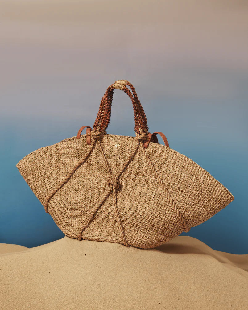 Woven straw handbag on a sandy surface with a blurred blue background