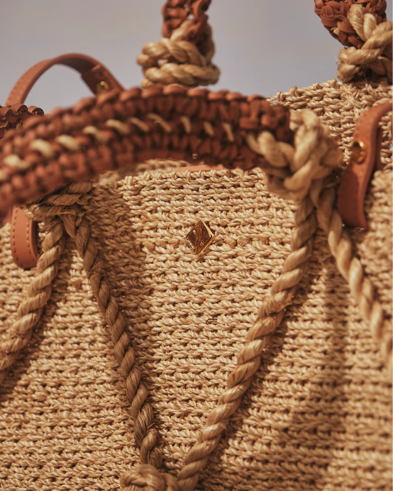 Close-up of a woven bag with braided handles and leather accents.
