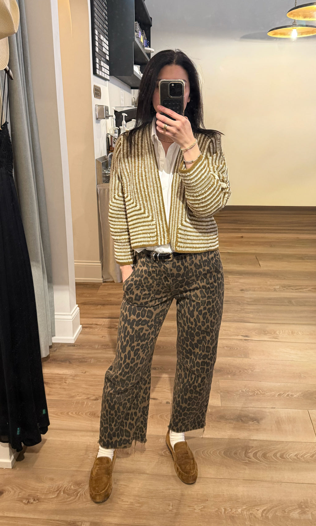 Person wearing a striped cardigan, white shirt, leopard print pants, and brown shoes in a room. Knit cardigan, hand woven knit cardigan, olive and white abstract knit cardigan. 