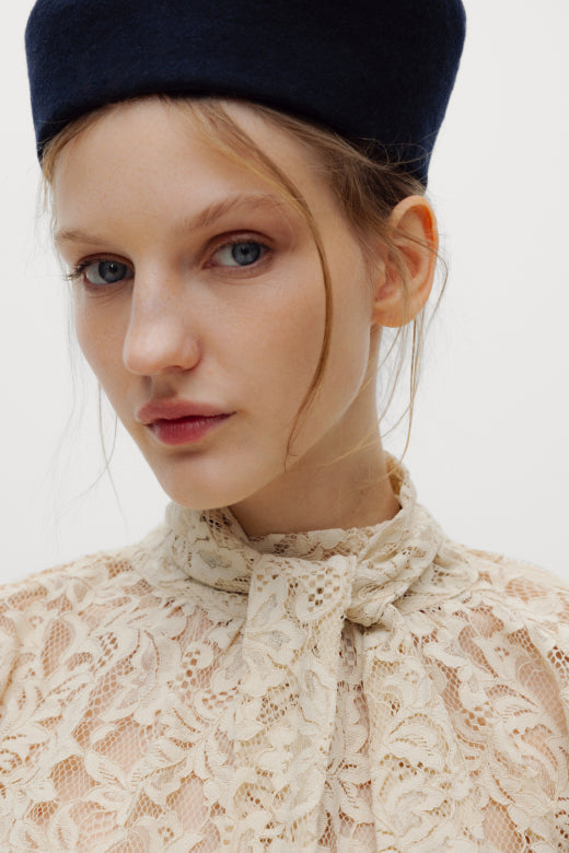 Woman wearing a navy hat and lace top against a white background