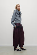 Woman wearing a gray sweater and burgundy pants against a white background