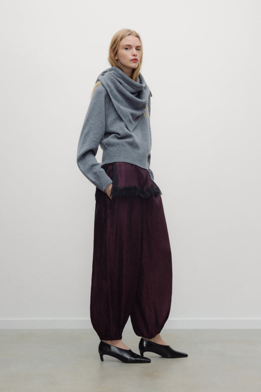 Woman wearing a gray sweater and burgundy pants against a white background