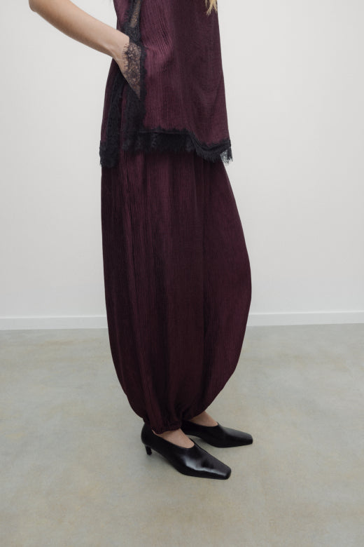 Person wearing a dark purple outfit with a matching scarf on a plain background