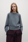 A model wearing a heather gray crewneck sweater and a dark burgundy skirt with black lace trim, standing against a plain light gray background.